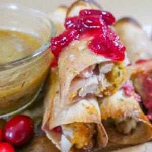 Thanksgiving leftovers taquito on a plate with gravy and cranberry sauce