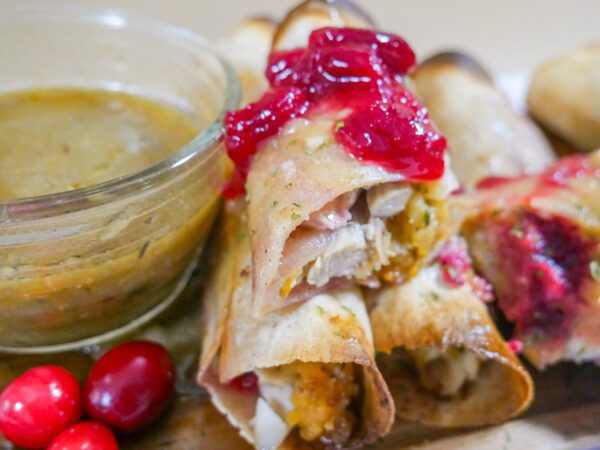 Thanksgiving leftovers taquito on a plate with gravy and cranberry sauce