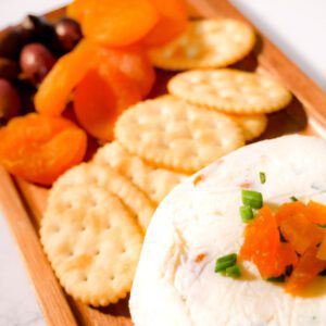 Apricot cheese on a platter with crackers, apricot and olives.