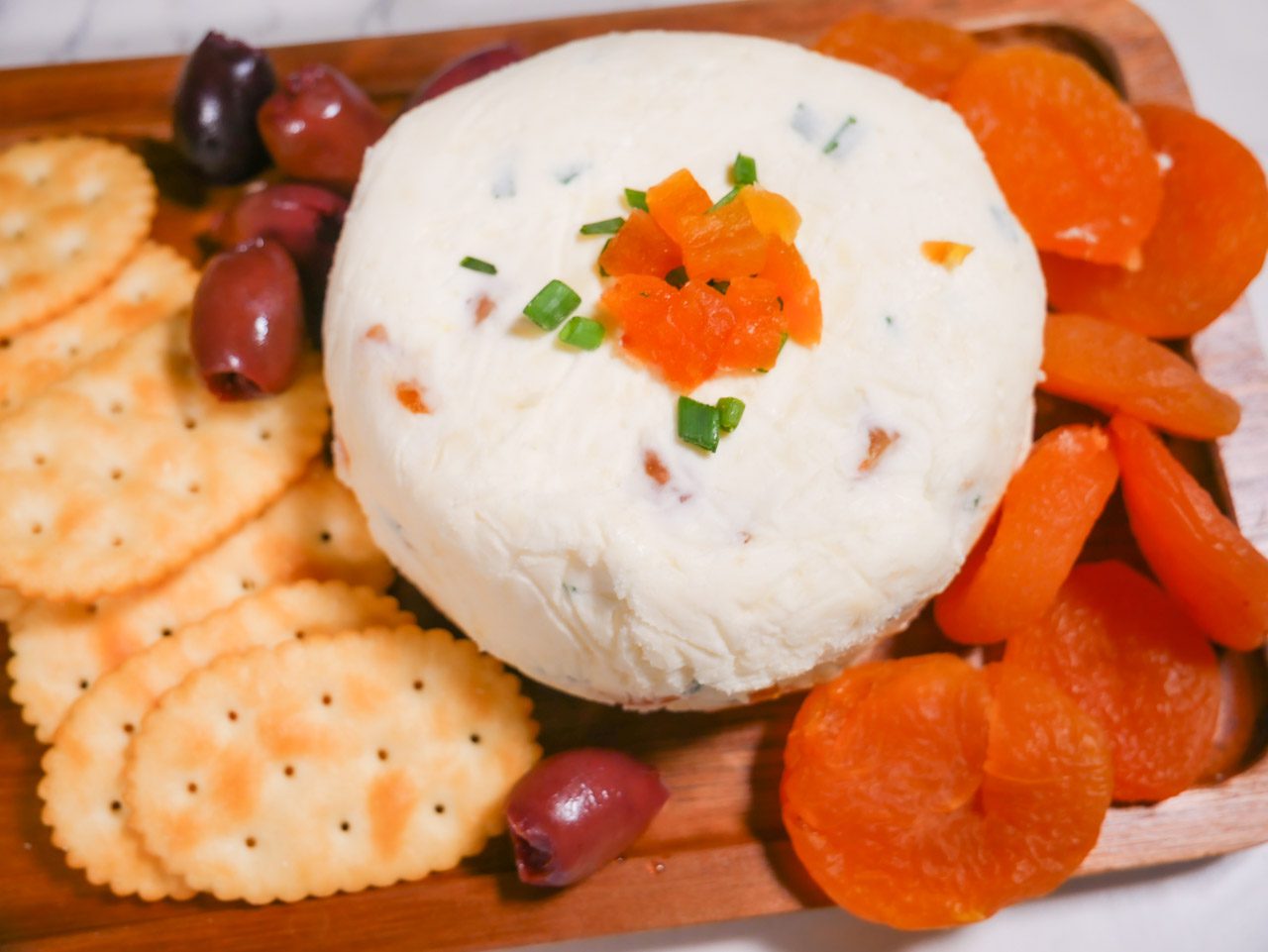Apricot cheese on a platter with crackers, apricot, and olives.