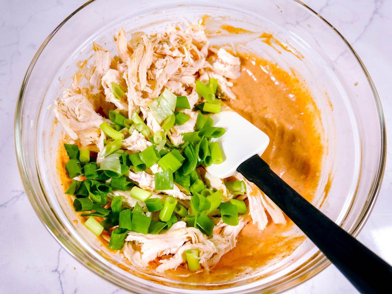 Green onions, chicken, and sauce ingredients mixed in a bowl with a rubber spatula. 