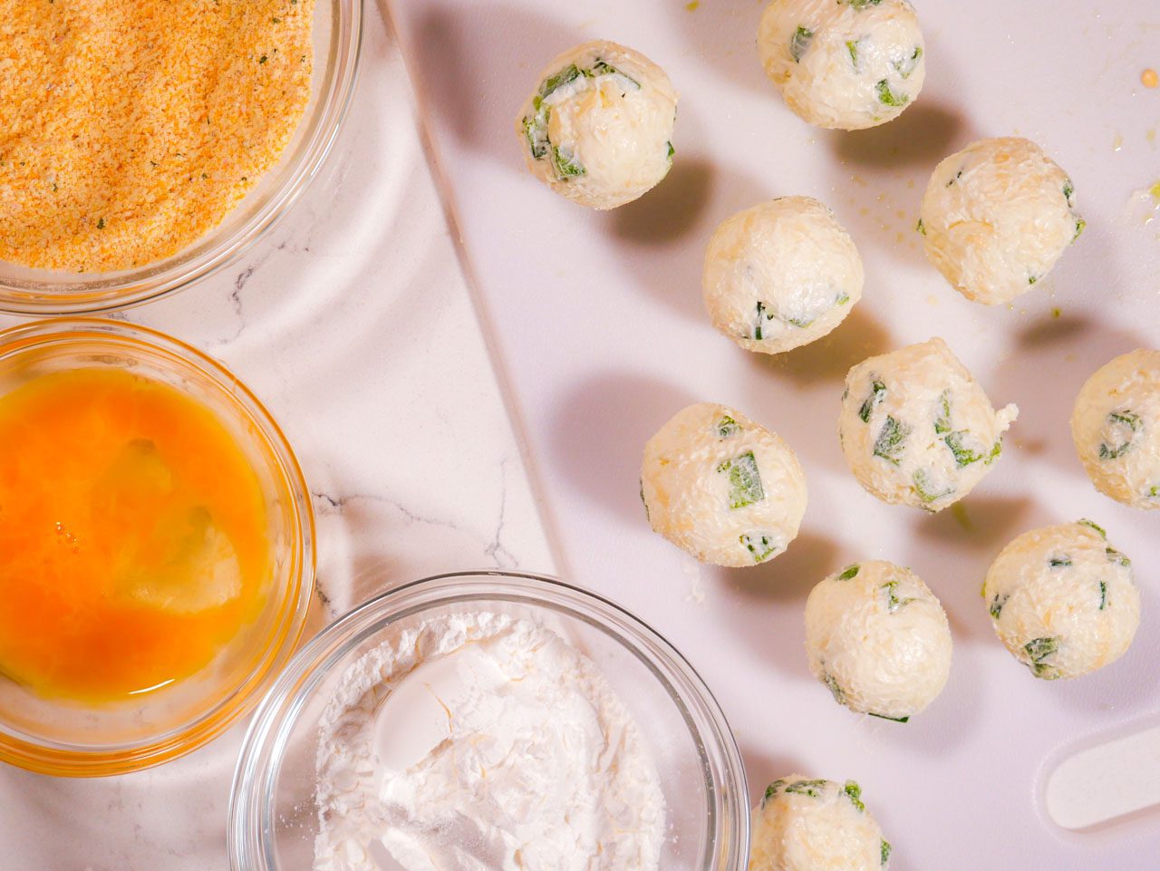 Jalapeno popper mixture formed into balls with cornstarch, egg wash, and cornmeal in bowls beside them