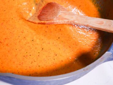 Roasted red pepper bisque cooking in pan with wooden spoon