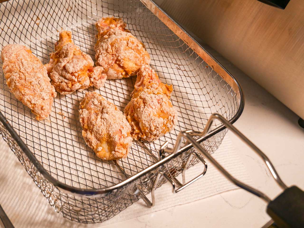 Breaded chicken wings in a fryer basket waiting to be fried
