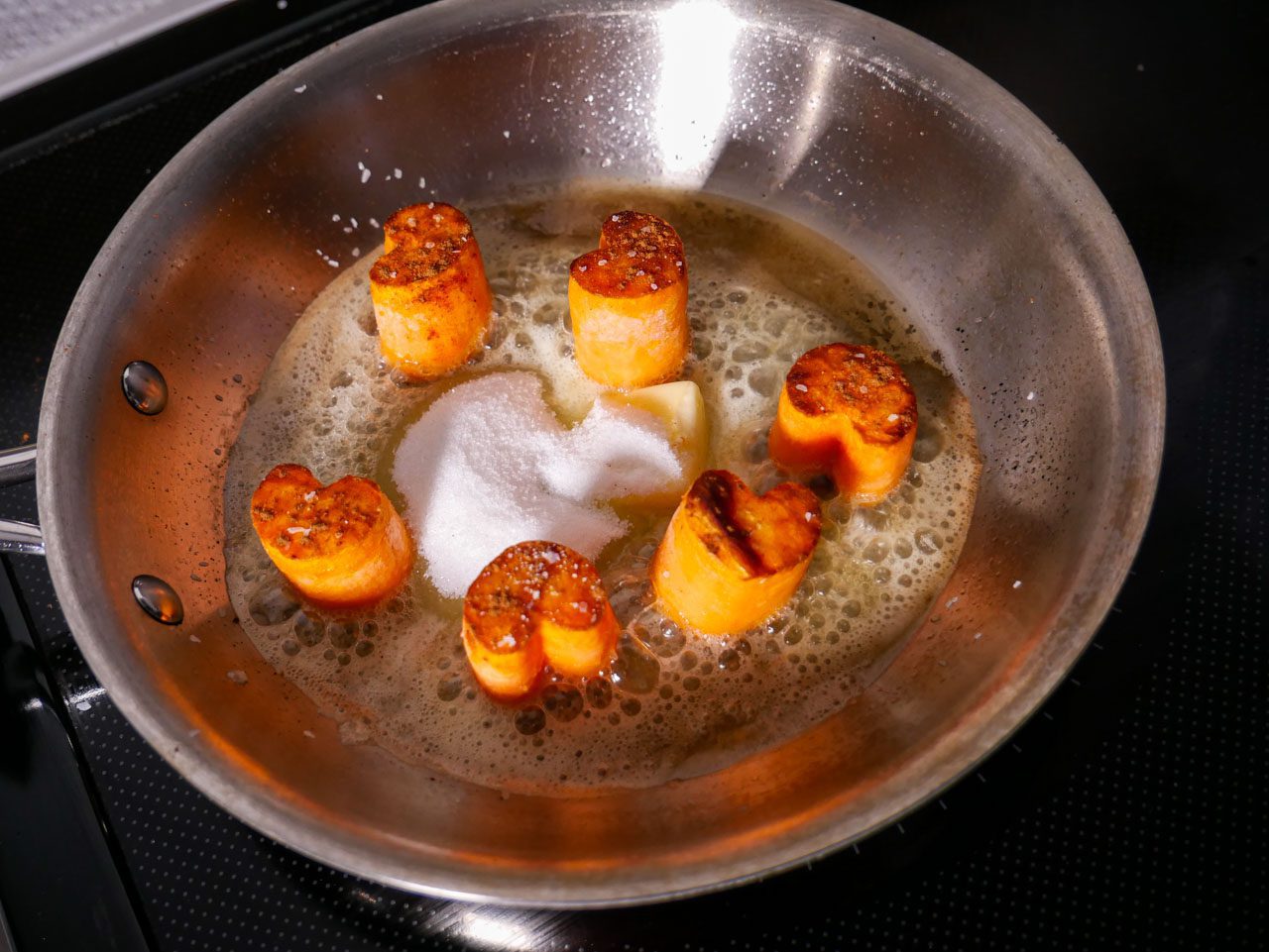Butter and sugar added to heart-shaped sweet potatoes in a frying pan