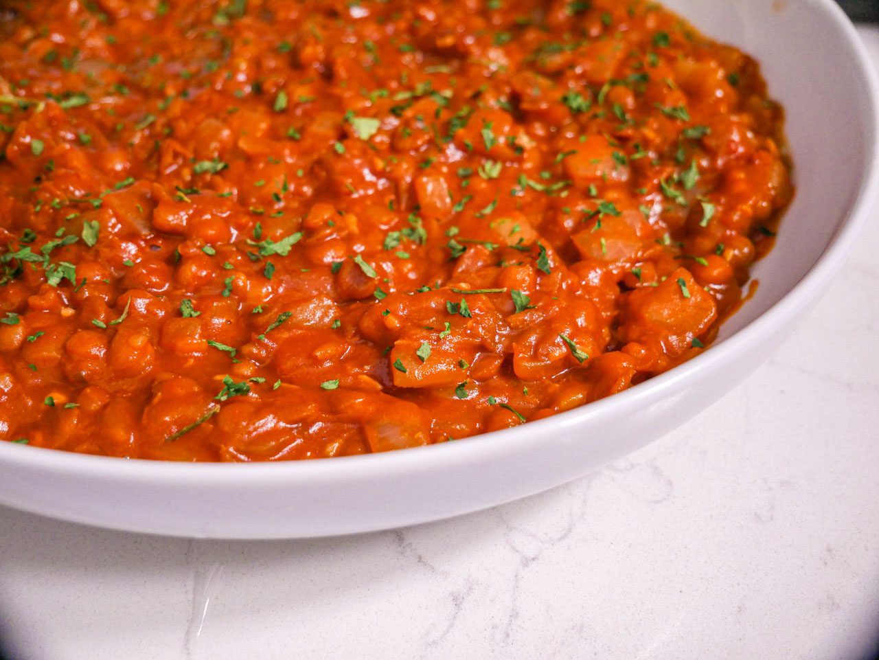 Hearty Savory Breakfast Lentils in a white bowl with parsley sprinkled on top