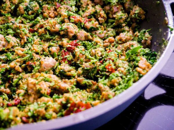 Veggie sausage crumbles in a blue pan on a black stove.