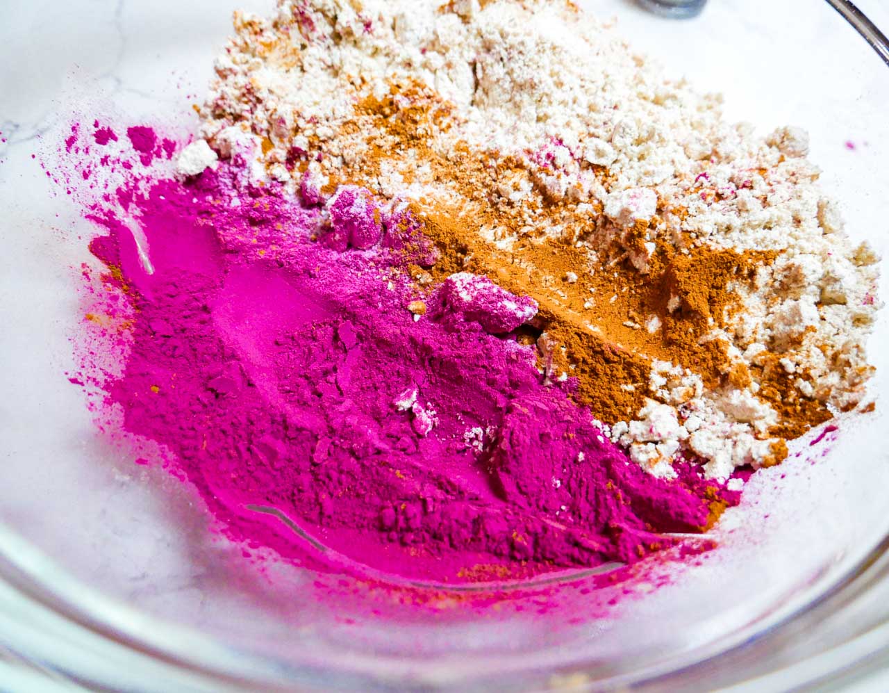 Dragon fruit powder with dry ingredients in a clear glass bowl on a white countertop