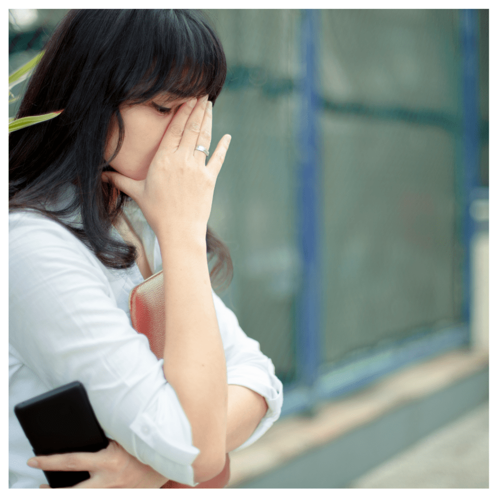 Woman hiding her face behind her hand against an office building. She is overwhelmed. Worst jobs for highly sensitive person