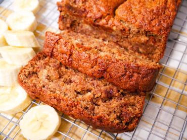 Tiger Nut Flour Banana Bread on a wire rack cooling with sliced bananas along the side of the bread. Place on yellow and white napkin.