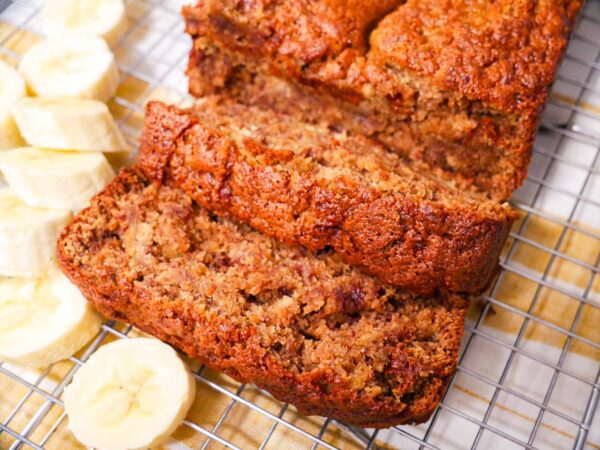 Tiger Nut Flour Banana Bread on a wire rack cooling with sliced bananas along the side of the bread. Place on yellow and white napkin.