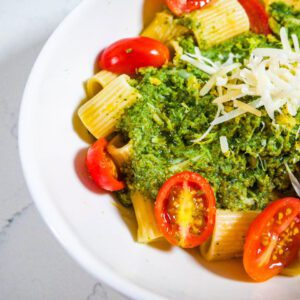 Veggie sauce on pasts with fresh grape tomatoes and shredded parmesan in a white bowl on white countertop.