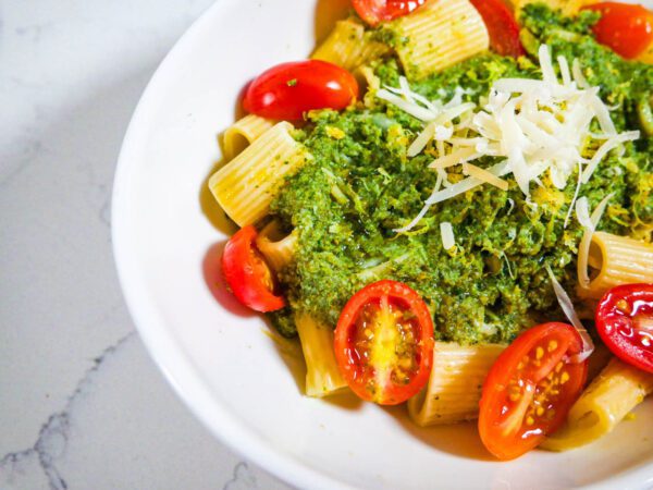 Veggie sauce on pasts with fresh grape tomatoes and shredded parmesan in a white bowl on white countertop.