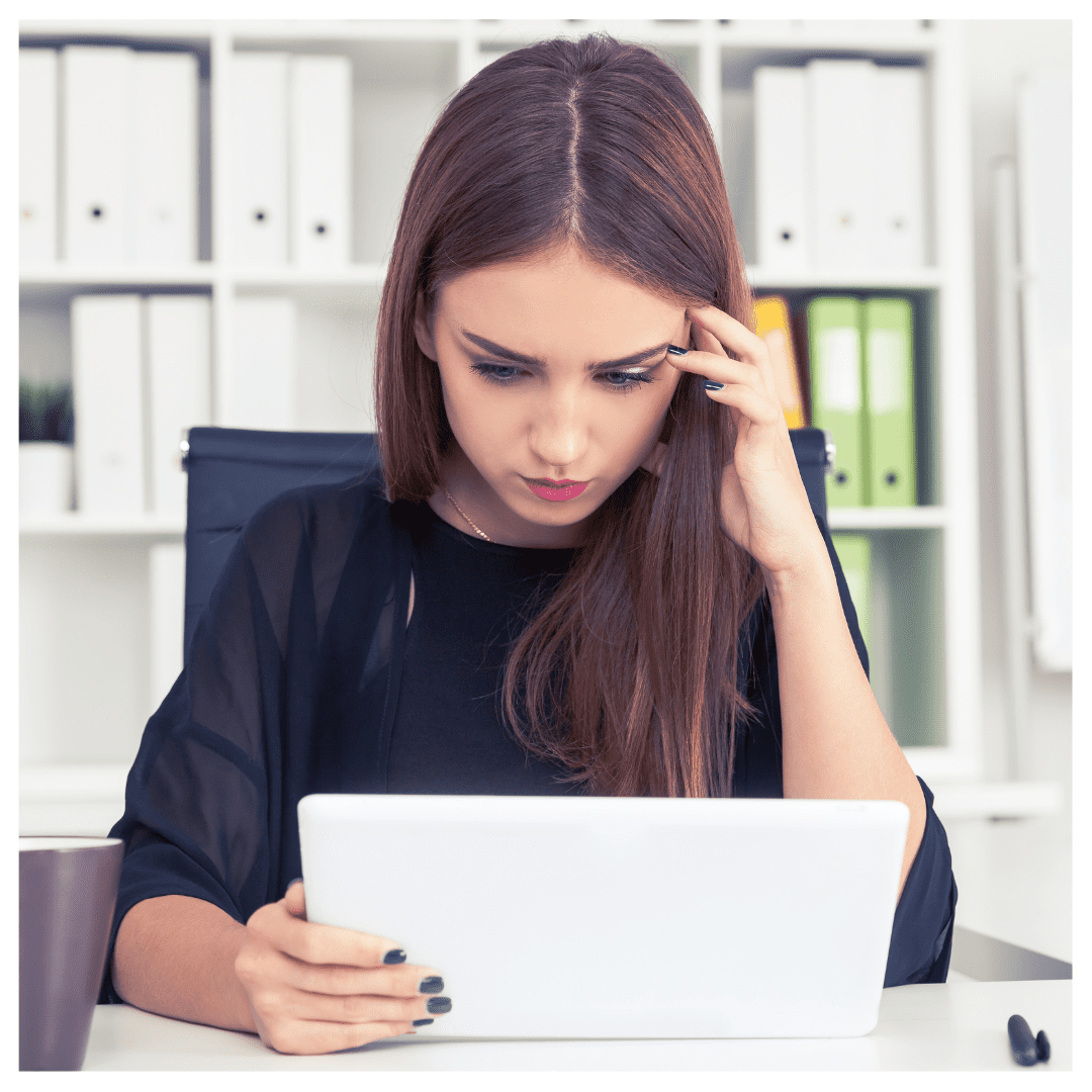 Letting go of perfectionism - woman staring at white laptop looking uneasy in an office space.