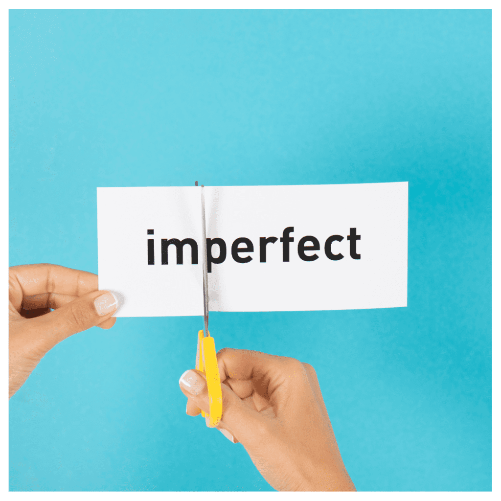 Letting go of perfectionism- hands holding a piece of paper that says "imperfect" and cutting the paper in between "I'm" and "perfect" against a turquoise background.