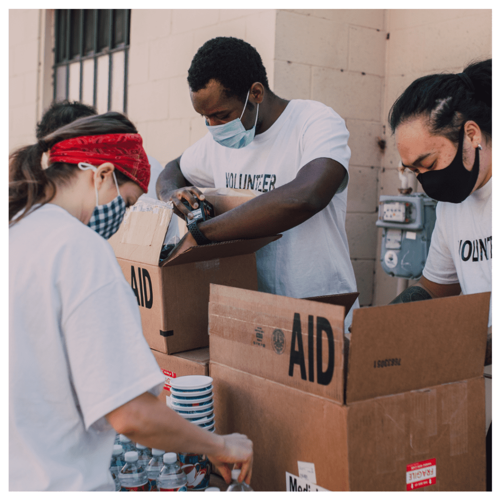 Three people showing kindness by packing boxes that says "Aid" with supplies to help others.