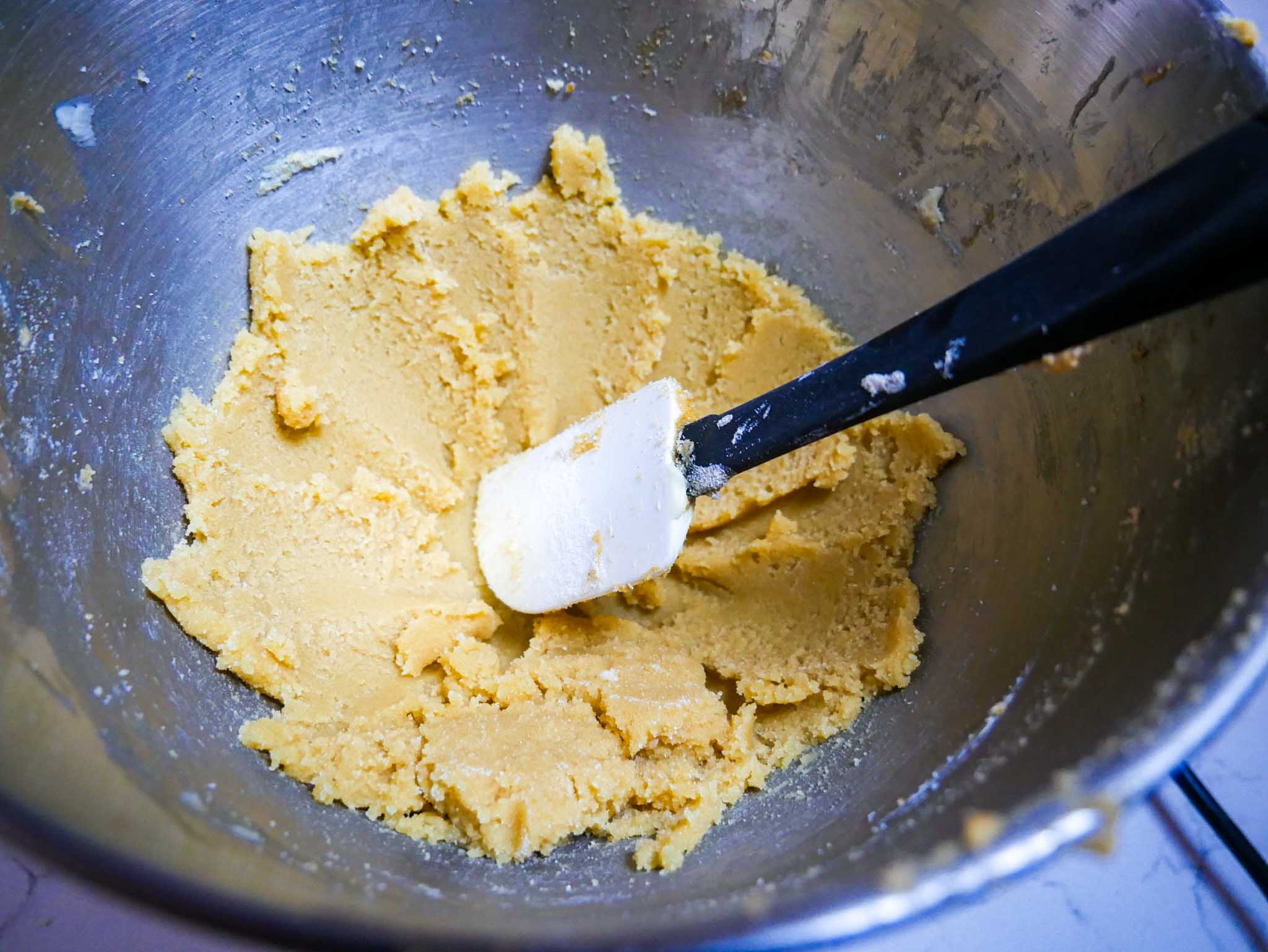 Creamed butter and sugars in a standing mixer bowl with a rubber spatula.