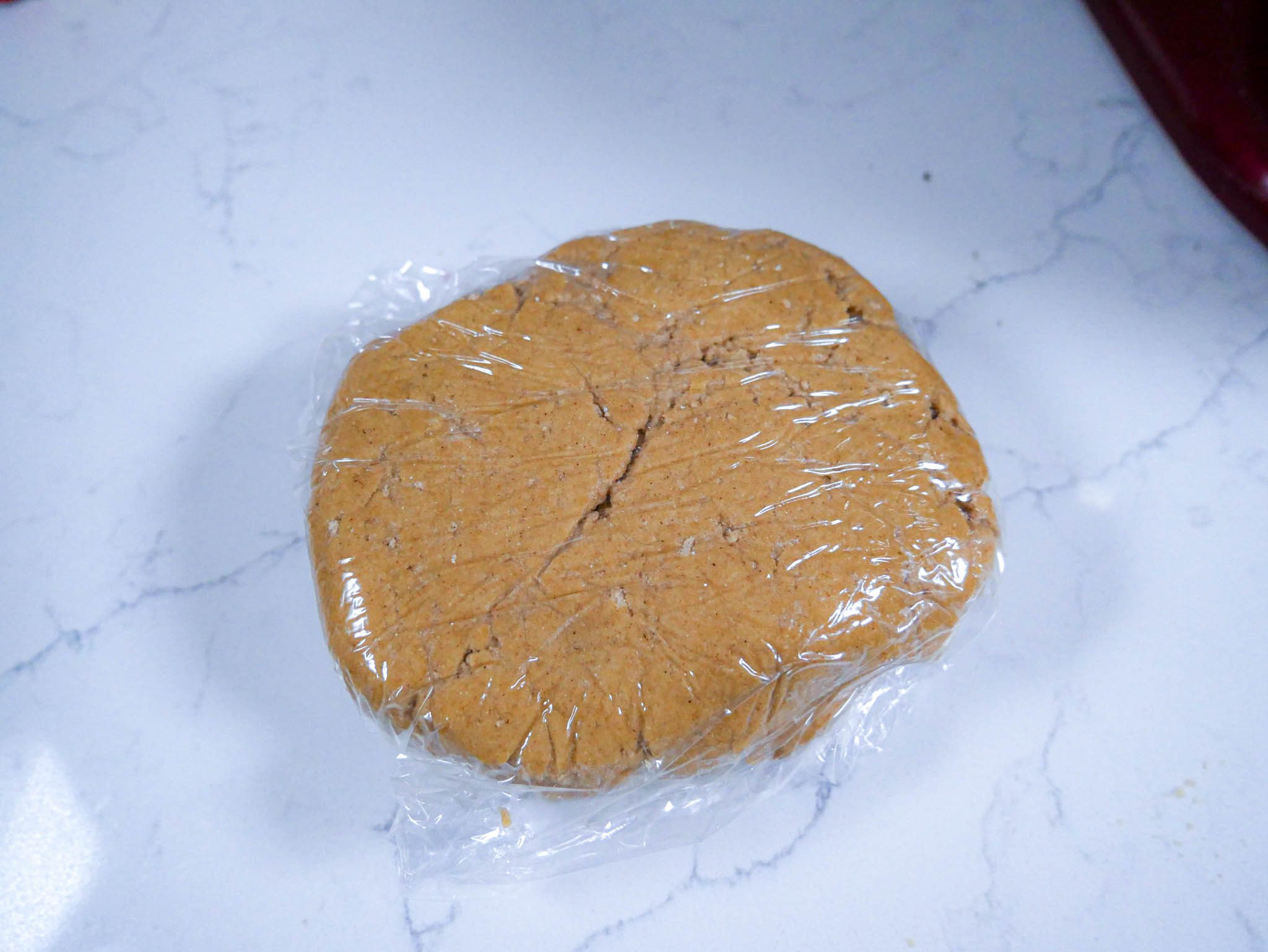 Mango lassi cookie dough wrapped inside a plastic cling wrap, rest on a white countertop.