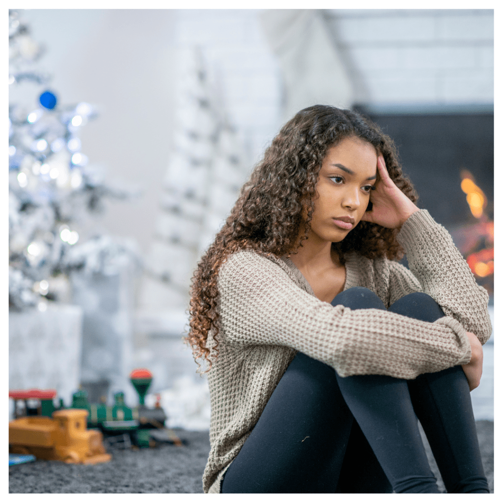 A teenager with holiday blues. White Christmas trees are in the background along with a fireplace. 